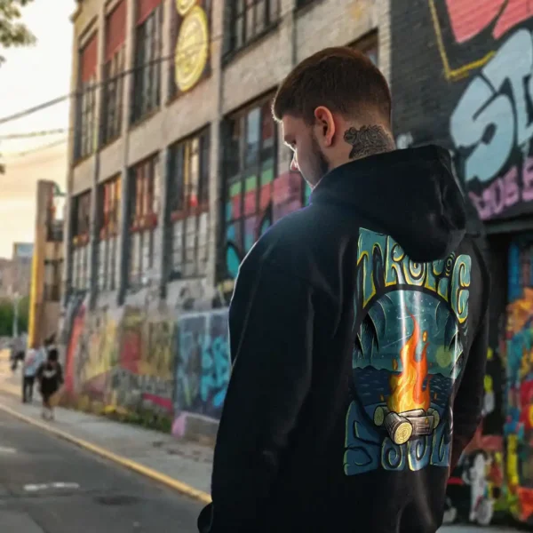 A male model with his back turned wearing a black tropic soul hoodie featuring the Moon Fire and night sky over the sea graphic.