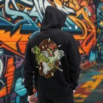 A male model with his back turned wearing a black Easy Days hoodie featuring a chicken skewered by a wooden stick and intestines graphic.