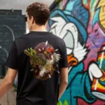 A male model with his back turned wearing a black Easy Days tshirt featuring a chicken skewered by a wooden stick and intestines graphic.