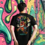 A male model with his back turned wearing a black Easy Days tshirt featuring a cow juggling spices and ingredients for an exotic soup with a bandaid on its crotch.