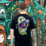 A male model with his back turned wearing a black Easy Days tshirt featuring a monsterfied balut egg graphic.