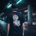 A male model with his back turned wearing a black Manifesto shirt featuring a man who seems like a statue, hands in a praying position, eyes staring at the skies above