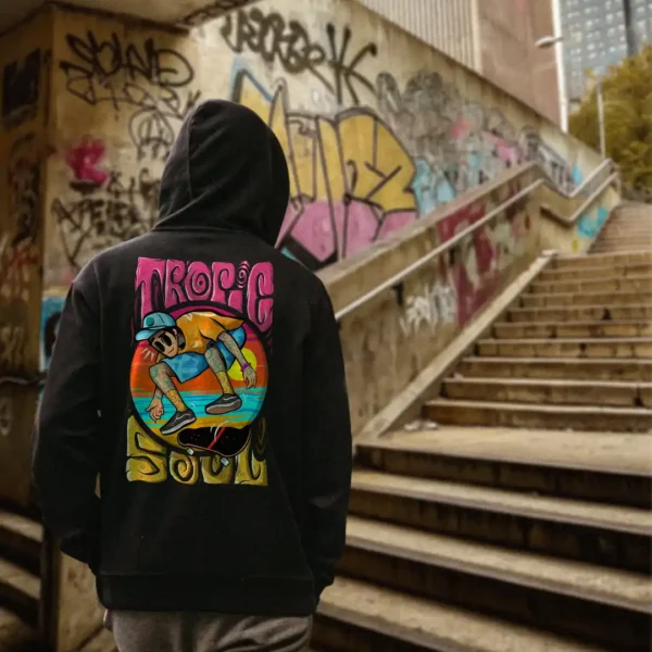 A male model with his back turned wearing a black tropic soul hoodie featuring the Flip Me skateboard and beach graphic.