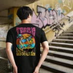 A male model with his back turned wearing a black tropic soul tshirt featuring the flip me skateboard and beach graphic.