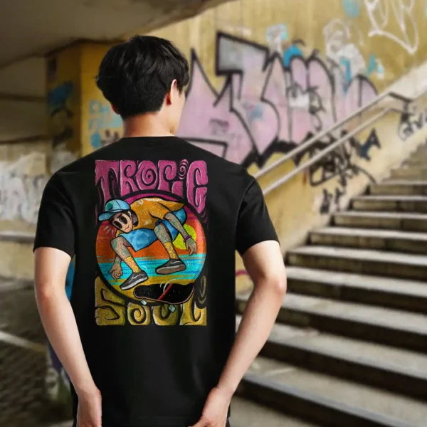 A male model with his back turned wearing a black tropic soul tshirt featuring the flip me skateboard and beach graphic.