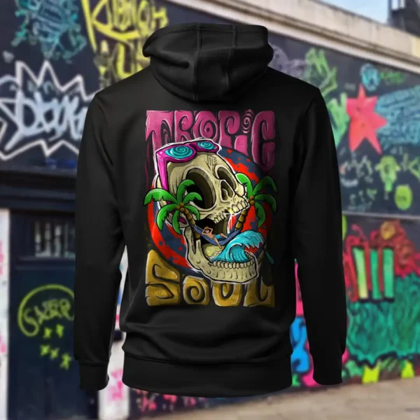 Back view of black Tropic Soul hoodie displaying a man relaxing on a hammock tied to the Skull Island's palm trees next to a giant wave rear graphic placement and hood detail.