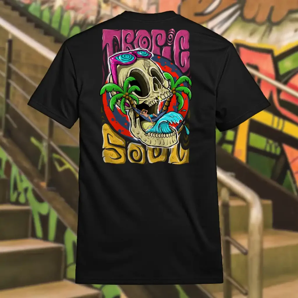 Back view of black Tropic Soul tshirt displaying a man relaxing on a hammock tied to the Skull Island's palm trees next to a giant wave rear graphic placement.