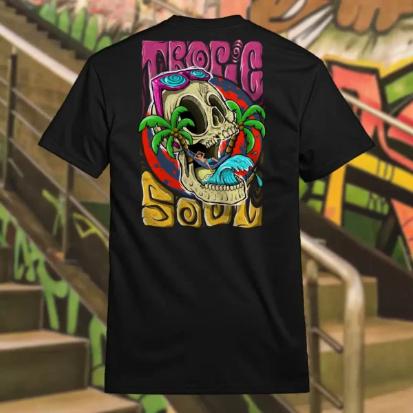 Back view of black Tropic Soul tshirt displaying a man relaxing on a hammock tied to the Skull Island's palm trees next to a giant wave rear graphic placement.