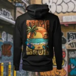 Back view of black Tropic Soul hoodie displaying the Sandset beach and waves rear graphic placement and hood detail.