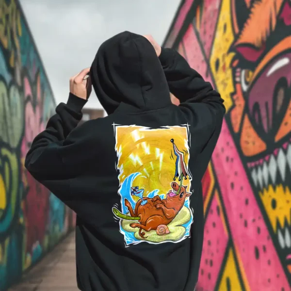 A male model with his back turned wearing a black Easy Days hoodie featuring a roasted pig skewered by a bamboo stick, lying underneath an umbrella taking cover from the sun.