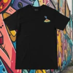 Front view of black tshirt featuring a roasted pig skewered by a bamboo stick, lying underneath an umbrella taking cover from the sun.