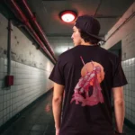 A male model with his back turned wearing a black Manifesto tshirt featuring a man falling back as he's impaled by a spear