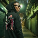 A male model with his back turned wearing a black Dark Fantasy hoodie featuring a warrior with eyes in his wings, a sword piercing through his head.