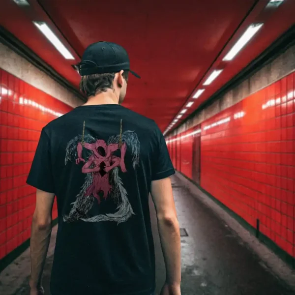 A male model with his back turned wearing a black Manifesto shirt featuring a red winged creature of dark, visibly hanged by ropes, opening its stomach with its unseen face